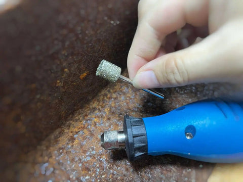 Hand using Pro Grade Diamond Grinding Burr Drill Bit Set One Eighth Inch Shank with blue rotary tool on rusted surface