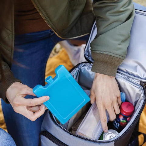 Person placing Maxcold Ice Block Four Pack Reusable Freezable Gel Cooling Blocks into lunch bag with drinks and snacks
