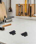 Two black Beefy Heavy Duty Shed Hinges For Barn Doors And Fence Gates on a workbench with tools in the background.