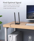 AX1800 USB WiFi 6 Adapter with 2 antennas on desk beside computer, USB cable connected to Windows PC tower.