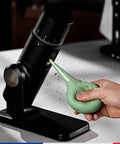 Hand using a green sparrow-inspired air blower on espresso machine, Dope Bird Inspired Coffee Air Blower Air Duster For Espresso Machines And Delicate Electronics Like Watches Cameras Keyboards And Sensors Removable Pump Cleaning Tool In White.