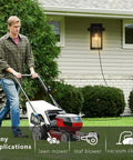 Man mowing lawn near black outdoor wall mount porch light with two built in GFCI outlets and weatherproof fixture for home