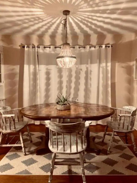 Wood Bead Chandelier Pendant For Boho Beachy Vibe Living Room Lighting hanging over a dining table, casting shadows on walls.