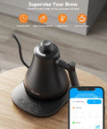 Smart Electric Kettle With WiFi And Alexa Control For Home Baristas Gooseneck Pour Over Kettle With Variable Temperature 1200W Quick Heat 0.8L Capacity One Hundred Percent Stainless Steel Matte Black on wooden table next to smartphone displaying control app.