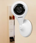 Wireless Security Camera E4 1080P HD Indoor WiFi Cam mounted on wall in home environment. Round lens design.