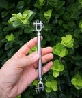Badass M6 Jaw And Jaw Turnbuckle Forged From 316 Stainless Steel Marine Grade Rigging Hardware Salt Water Resistant Comes With Locking Nuts held in hand among greenery.