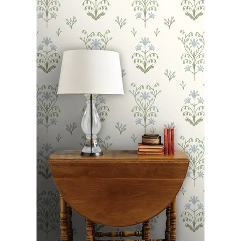 Premium Floral Meadow Wallcovering With A Subtle Matte Linen Texture Hits Different Across Every Room Built Tough For Busy Households Featuring No Sweat Paste To Paper Install on a living room wall with lamp and books.