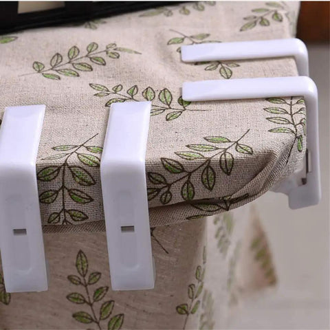 Four white 12 Pcs Plastic Spring Tablecloth Clips For Outdoor Tables No Slip Grip Easy Clamp Table Cloth Holders on a linen table cover.