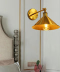 Built Tough Industrial Metal Swing Arm Wall Sconce Adjustable E27 Light Fixture Reinforced Mount with gold cone shade in bedroom.