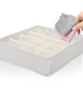 Hand placing rolled socks into Super Slick 16 Compartment Foldable Drawer Storage Box For Underwear And Socks Made From Soft Cotton Linen Blend In Warm Beige.