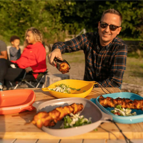 Person serving food into the Six Piece Camping Mess Kit With Plate Bowl Cup Switch Spork Utensil Set And Tether.