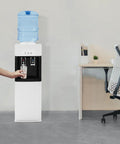 Person using hot and cold water dispenser with five gallon top loading electric heater and cooler next to office desk