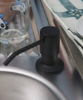 Built In Kitchen Sink Soap Dispenser Black Matte With Stainless Steel Pump next to a glass on a kitchen counter