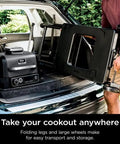 Person loading Woodfire Collapsible Outdoor Grill Stand For OG700 OG300 OO101 Series into car trunk for on-the-go grilling.