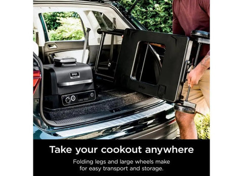 Person loading Woodfire Collapsible Outdoor Grill Stand For OG700 OG300 OO101 Series into car trunk for on-the-go grilling.