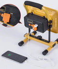 JUDYSSY Home Floodlight with USB charging port, adjustable stand, showing connection to a smartphone for emergency use.
