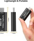 Hand holding black HDTV video capture device showing USB input and output, dimensions 6.3cm x 2.8cm x 1.3cm, labeled Lightweight & Portable.