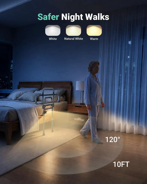 One Hand Fold Bed Rail For Seniors illuminated in adjustable light options beside bed with a person walking at night.