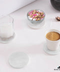 Set Of Six Round Marble Coasters With Secure Holder White Polished Stone For Kitchen Countertops, coffee cup and candle on coasters.