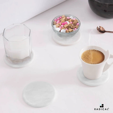 Set Of Six Round Marble Coasters With Secure Holder White Polished Stone For Kitchen Countertops, coffee cup and candle on coasters.