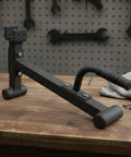 Heavy Duty Barbell Plate Lifter And Plate Change Jack with curved handle on wooden table in workshop setup.