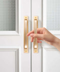 Close-up of hand on 2 Pack Barn Door Handles for Cabinets and Drawers, Aluminum Alloy Flush Flat Base Pulls in Gold, installed on white door.