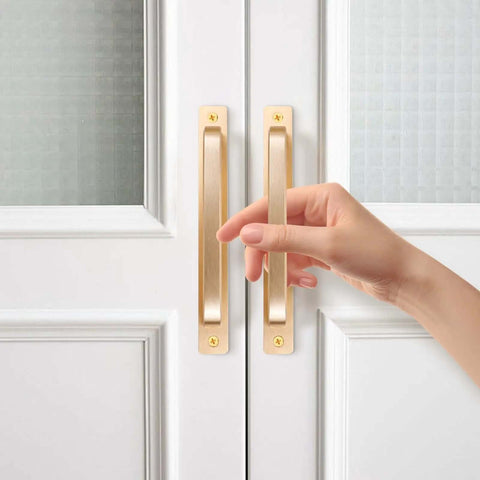 Close-up of hand on 2 Pack Barn Door Handles for Cabinets and Drawers, Aluminum Alloy Flush Flat Base Pulls in Gold, installed on white door.