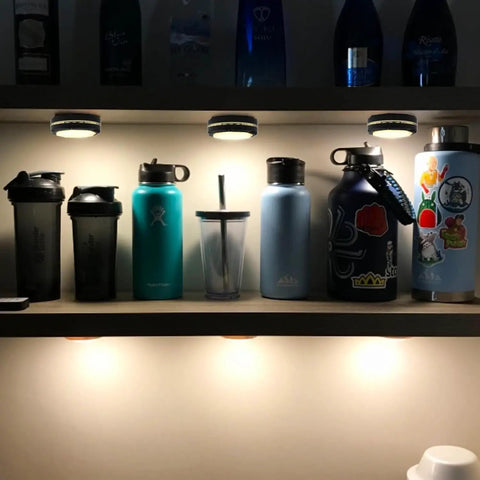Rechargeable USB Puck Lights For Under Cabinet And Closet, 16 Color Changing Dimmable LEDs illuminating water bottles on shelf.