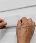 Hands applying patch from Vinyl And Stucco Siding Repair Kit With White Self Adhesive Patches That Cut To Fit Paintable To Match Cover Cracks Holes And Blemishes Weather Resistant Indoor Outdoor Use Includes 2 Patches on white siding.