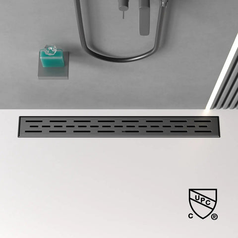 24 Inch Black Linear Shower Drain With Brickwork Cover in bathroom setting on white floor, UPC symbol visible.