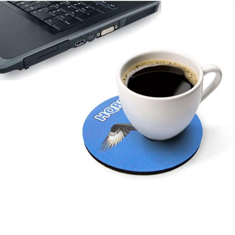 White coffee cup on round blue coaster near laptop