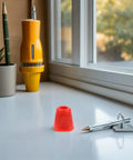 Red cone-shaped object on a white desk near a pen and key with window view