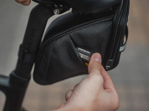 Close-up of hands interacting with the Aero Wedge Pack DX Medium Under Saddle Bag 0.9 L Expanding Capacity With QuickClick F25 Mount.