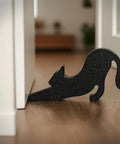 Black Eco Friendly Door Stopper with soft impact absorbing block shaped like a stretching cat, placed under a white door.