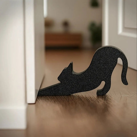 Black Eco Friendly Door Stopper with soft impact absorbing block shaped like a stretching cat, placed under a white door.