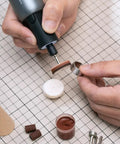 Close-up of a hand using a rotary tool; Badass Sixty Piece Rotary Tool Accessory Crate For One Eighth And Three Thirty Two Shafts.