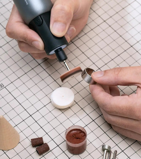 Close-up of a hand using a rotary tool; Badass Sixty Piece Rotary Tool Accessory Crate For One Eighth And Three Thirty Two Shafts.