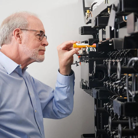 Fluke FiberLERT-125 fiber optic tester (orange) being used by technician at a server rack.