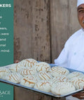 Baker holding a full sheet tray with baked goods, showcasing Saffron & Sage bakeware, with text explaining the brand's roots and quality focus.