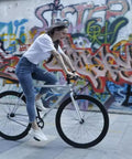 Woman riding a single-speed bike, showcasing Chain Master Link For Bicycle Chains Half By Eighth Quick Release Connector Compatible With Single Speed BMX Fixie And Some Mountain Bikes 6 Pack Silver Built Tough Easy Installation in urban graffiti setting.