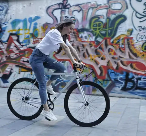 Woman riding a single-speed bike, showcasing Chain Master Link For Bicycle Chains Half By Eighth Quick Release Connector Compatible With Single Speed BMX Fixie And Some Mountain Bikes 6 Pack Silver Built Tough Easy Installation in urban graffiti setting.