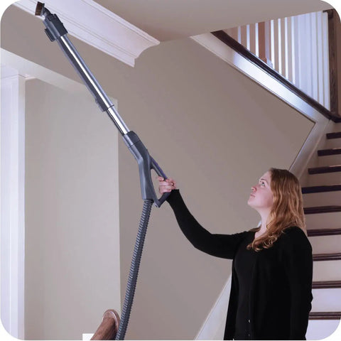 Woman using Heavy Duty Bagged Canister Vacuum on ceiling corner; swivel head for easy navigation and cleaning.