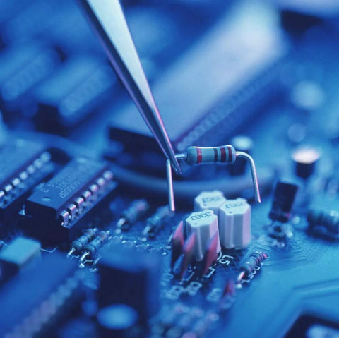 Axial resistor with color bands, close-up view held by tweezers over a blue circuit board