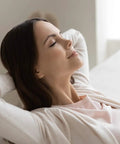 Person relaxing on a white sofa in a bright living room, enjoying clean air from 24 Pack 4x10 Floor Vent Register Filters for easy home use.