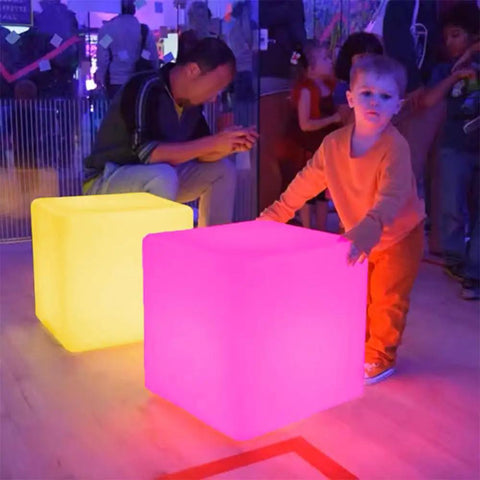 15 Inch RGB LED Cube Light With Remote Color Changing Cubes as seating in a lively indoor setting, glowing yellow and pink.