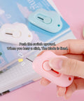 Hand holding pink cutter from 9 Pack Retractable Box Cutter Set With Mini Letter Opener And Cute Cloud Charm, showing blade extended.