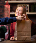 Person handing over a Brown Kraft Gift Bag With Handles 5x3x8.25 Inches Bulk Pack 750 Small Paper Bags for Gifting.