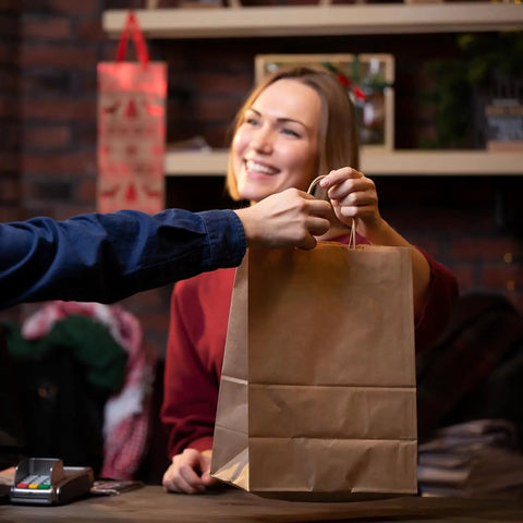 Person handing over a Brown Kraft Gift Bag With Handles 5x3x8.25 Inches Bulk Pack 750 Small Paper Bags for Gifting.