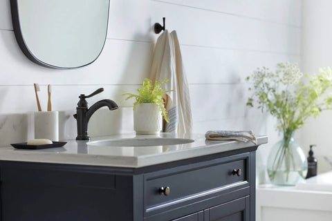 Elmhurst Handle Bath Faucet Oil Rubbed Bronze For One Or Three Hole Four Inch Install Includes Optional Deck Plate And Fifty Fifty Pop Up Drain ADA Compliant And WaterSense Labeled For Efficient Water Use in bathroom setting on vanity with plants.