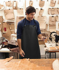 Man wearing Heavy Duty PU Apron And Latex Gloves Set For Kitchen And Lab Use, standing in a workshop with leather tools.
